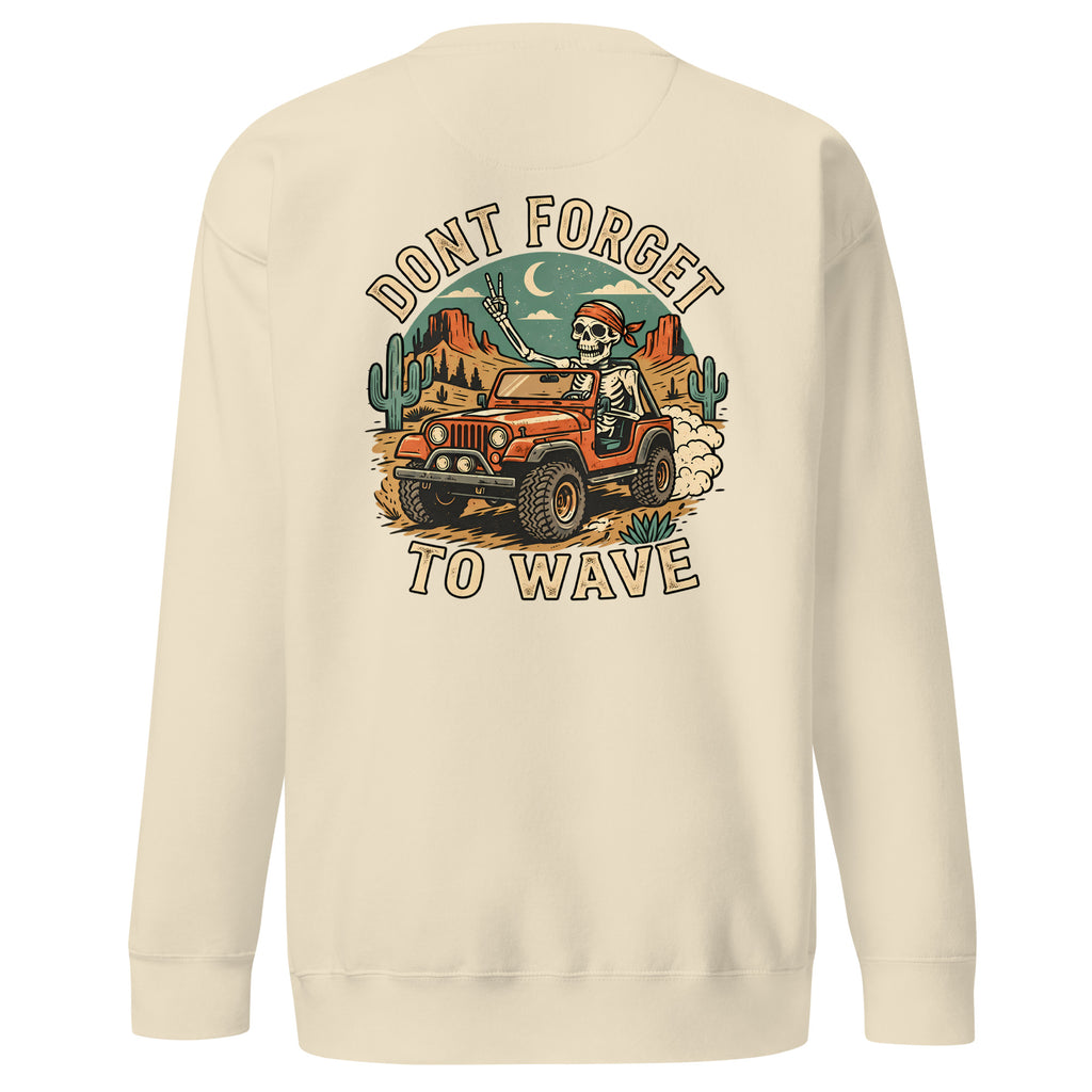 A cream-colored crewneck sweatshirt shown from the back, featuring a large graphic print of a skeleton driving an orange jeep through a desert landscape with cacti and the text 'DONT FORGET TO WAVE'.